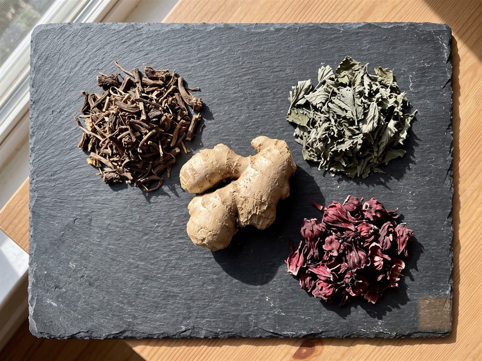 Dried dandelion root, nettle and hibiscus with fresh ginger on dark slate