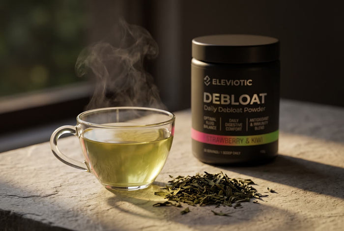 A cup of green tea and loose leaves beside a tub of Debloat in warm side light